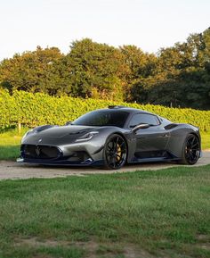 a grey sports car parked on the side of a road next to a field and trees