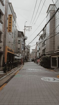 an empty city street with power lines above it and buildings on both sides in the distance