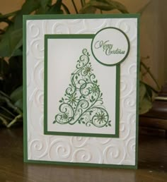 a card with a christmas tree on it sitting on a table next to a potted plant