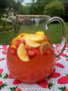 a pitcher filled with fruit sitting on top of a table covered in red and white cloth