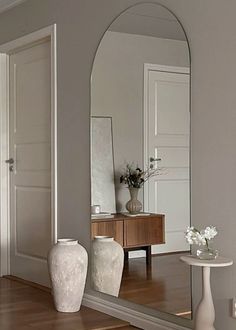 a large mirror sitting on top of a wooden floor next to a white vase filled with flowers