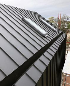 a black metal roof with a skylight on it's side and another building in the background