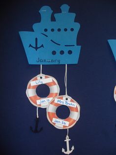 two paper boats and an anchor hanging from hooks with name tags in front of them