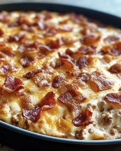 a close up of a pizza in a pan on a table with cheese and bacon