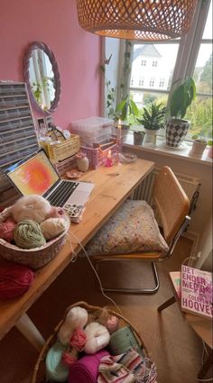 a wooden desk topped with a laptop computer next to a basket filled with balls of yarn