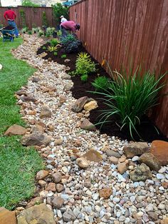 a garden with rocks and plants next to a fence