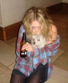 a woman sitting on the floor holding a dog and drinking from a beer bottle in her hands