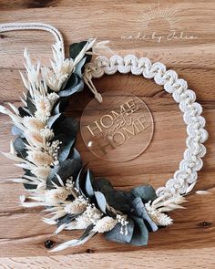 a wreath made out of white flowers and greenery on a wooden surface with the words home is where i belong