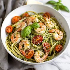 a white bowl filled with pesto pasta and shrimp on top of a marble table