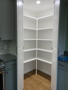 an empty pantry with white shelving in the corner and wood flooring on the other side