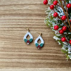 two pairs of earrings sitting on top of a wooden table next to a christmas tree