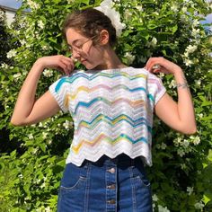 a woman standing in front of flowers wearing a crochet top and denim skirt