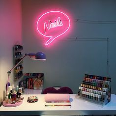 a pink neon sign that says nails on the wall next to a desk with supplies