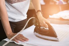 a woman ironing fabric with an electric iron on the table in front of her