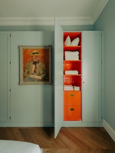 a bedroom with a painting on the wall next to an orange dresser and white bed