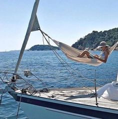 a woman laying in a hammock on top of a sailboat near the ocean