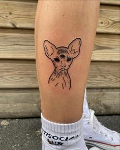 a small tattoo on the leg of a person with a cat's head in black ink