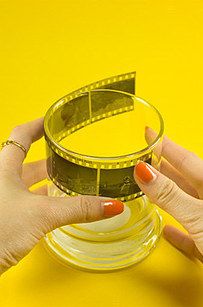 two hands holding up a small glass with film strips on the rim, against a yellow background