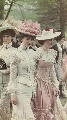 In the midst of a lush, green park, three women display the height of Victorian-era fashion with their elegant dresses and elaborately decorated hats. Each dress, adorned with laces, ribbons, and ruffles, reflects the intricate styles of the late 19th century. As they stand side-by-side, their poised demeanor and the soft, muted colors of their outfits together evoke a sense of timeless grace and sophisticated social interaction typical of their era. 1900s British Fashion, Victorian Era England, Victorian Era Fashion Woman, Victorian England Fashion, 1900 Outfits, Neo Victorian Fashion, 19th Century Fashion Women, Decorated Hats, 1800 Fashion