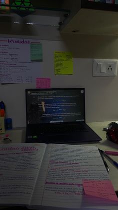 a laptop computer sitting on top of a desk next to an open book and pen