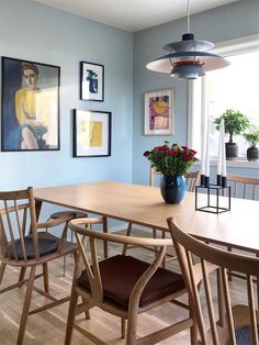 a dining room table with chairs and pictures on the wall above it, along with two vases filled with flowers