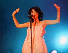 a woman in a pink dress holding her arms up and singing into a microphone on stage