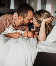 a man and woman laying in bed with a baby on their lap, looking at each other