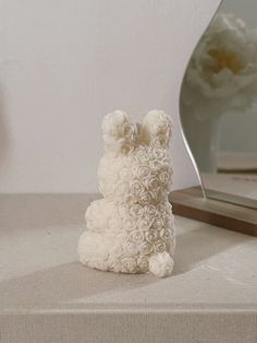 a white teddy bear sitting on top of a table next to a mirror and vase