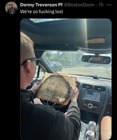 a man driving a car while holding a large piece of bread in his hand and looking at the camera