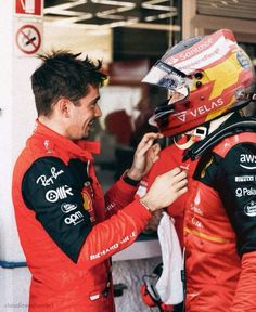 two men standing next to each other on top of a race track wearing red and black uniforms