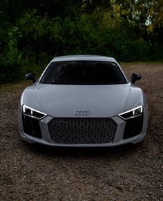 the front end of an audi sports car parked on gravel road with trees in background