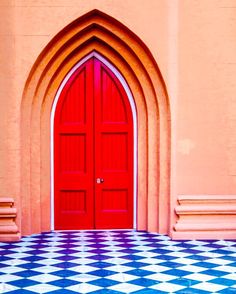 a red door with a checkered floor in front of an arched entrance to a building