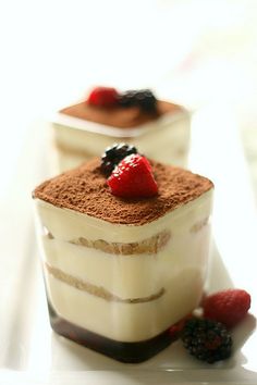 two desserts are sitting on a white surface with berries and chocolate sauce in the middle