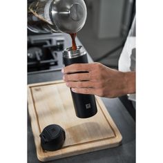 a person pouring something into a cup on top of a cutting board