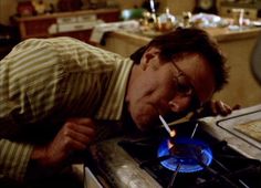 a man leaning over to look at a blue flame on a stove top burner