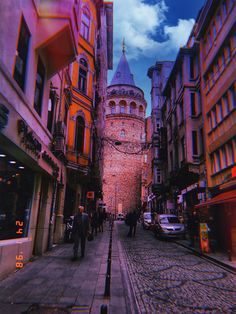 people are walking down the street in an old city with tall buildings on either side