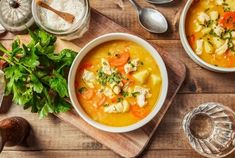 two bowls of soup are sitting on a wooden table next to silverware and spoons