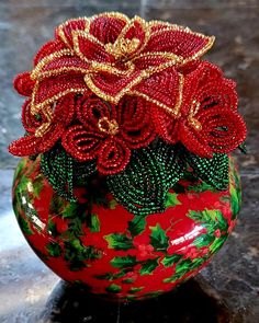 a red vase filled with lots of flowers on top of a marble counter covered in gold and green beads