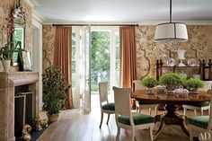 the dining room is decorated with floral wallpaper and green velvet upholstered chairs