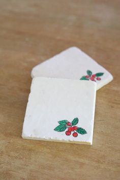 two white coasters with holly designs on them sitting on a table top next to each other