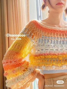 a woman is standing in front of a window with her hands on her hips and wearing a multicolored crocheted sweater