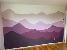 an empty room with mountains painted on the wall and wood flooring in front of it