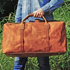 An extra-large duffle, crafted from the finest, vintage-appearing leather, this highly functional duffle bag is designed to tote everything from clothing to a laptop. It is large enough for storing a laptop (up to 17''), clothing, and shoes. It has double zips top open and a side pocket. It also has other interior pockets for storing things like your charger and mobile phone. Its shoulder strap is adjustable and removable. Outer 100% vegetable tanned, worn look, genuine cowhide leather. Inner 100% cotton cloth lined. YKK zipper. This bag is a unisex bag. Wipe clean with damp cloth. Use professional leather caring kit. Rugged Weekender Bag With Luggage Sleeve For Everyday, Rugged Everyday Duffle Bag With Luggage Sleeve, Rugged Rectangular Travel Bag For Everyday Use, Rugged Rectangular Everyday Travel Bag, Rectangular Rugged Travel Bag, Rectangular Waxed Finish Weekender Bag For Weekend Trips, Rectangular Oiled Leather Travel Bag, Rugged Large Capacity Rectangular Travel Bag, Rugged Large Capacity Weekender Bag For Everyday Use