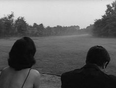 two people sitting on a bench looking out at the field and trees in the distance