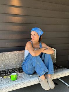 a woman sitting on a bench with her legs crossed and wearing a blue bandana