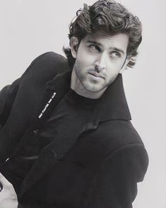 a man with curly hair wearing a black jacket and posing for a photo in front of a white background