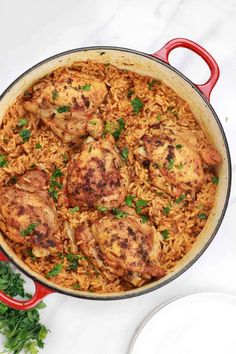 chicken and rice with parsley in a red pan on a white countertop next to two plates