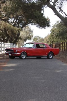 a red car is parked on the side of the road near some trees and fence