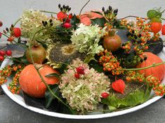 a white bowl filled with lots of different types of flowers and fruit on top of a table