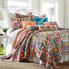 a bed covered in lots of colorful comforters and pillows on top of a wooden floor